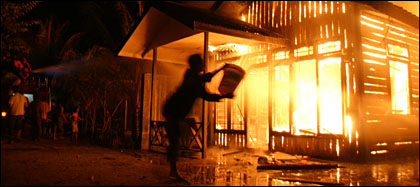 Seorang warga menyiramkan air dengan menggunakan ember ke arah rumah yang dilalap api