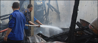 Petugas PMK menyemprotkan air ke puing-puing yang masih membara di salah satu gedung kantor milik Dinas PU Kukar