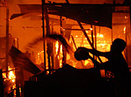 Seorang warga menyiramkan air ke arah api yang masih berkobar