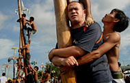 Seorang peserta pria berupaya menahan beban rekan-rakannya sambil memeluk batang pinang