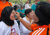 Dengan mata tertutup, seorang ibu merias wajah rekannya