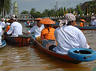 Para petugas yang membagikan kue gratis mengenakan pakaian daerah sambil menaiki perahu menyusuri Sungai Tenggarong