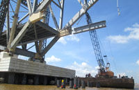 Sebuah crane di atas ponton mengangkat sebuah balok baja untuk penyangga lantai jembatan 