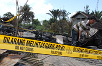 Pihak kepolisian memasang garis polisi di sekitar puing-puing rumah yang menjadi titik awal terjadinya kebakaran