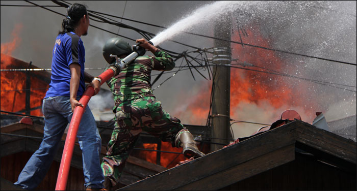 Seorang anggota TNI dibantu warga menaiki atap untuk menyemprotkan air ke arah kobaran api